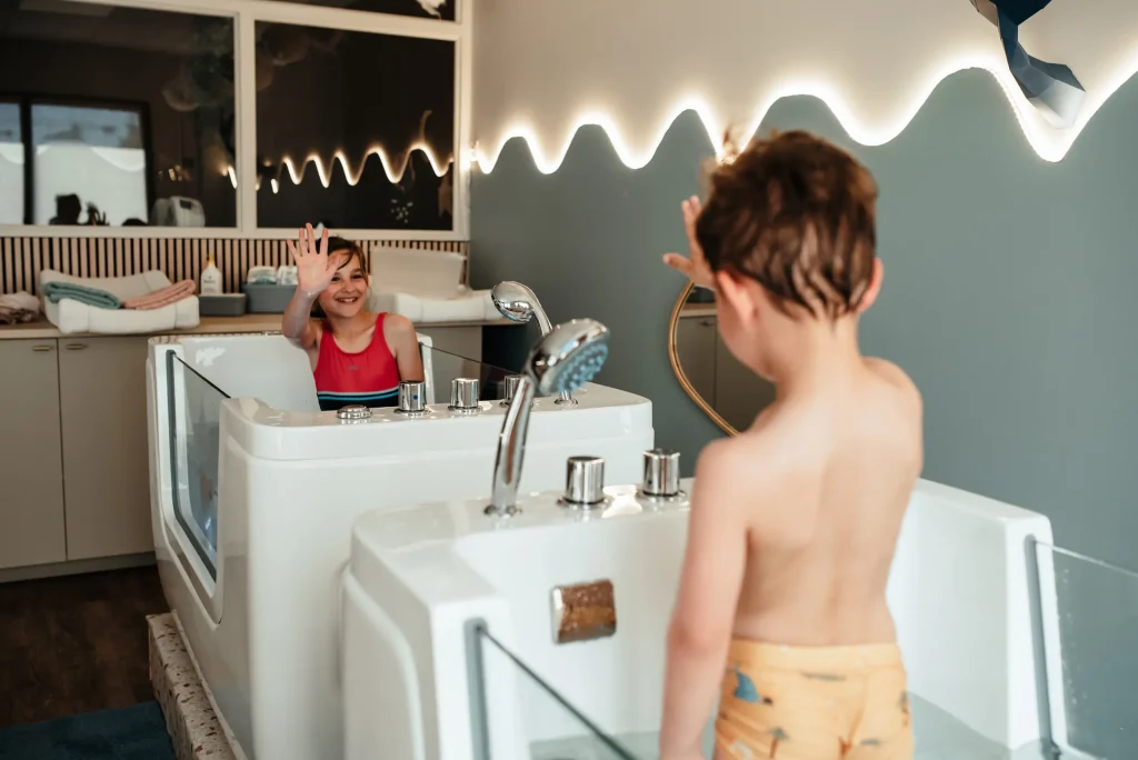 Deux enfants se faisant coucou d'une baignoire à l'autre pendant une séance Kids Spa en duo